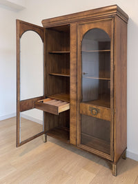 This beautiful art-deco arched glass and wood bookcase or curio cabinet is manufactured by the reputable B.P. John from Portland, Oregon. This piece is in such beautiful condition and the amazing arched doors and original brass hardware is a show-stopper for any style of home, office or commercial space.