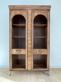 This beautiful art-deco arched glass and wood bookcase or curio cabinet is manufactured by the reputable B.P. John from Portland, Oregon. This piece is in such beautiful condition and the amazing arched doors and original brass hardware is a show-stopper for any style of home, office or commercial space.