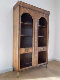 This beautiful art-deco arched glass and wood bookcase or curio cabinet is manufactured by the reputable B.P. John from Portland, Oregon. This piece is in such beautiful condition and the amazing arched doors and original brass hardware is a show-stopper for any style of home, office or commercial space.