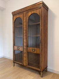 This beautiful art-deco arched glass and wood bookcase or curio cabinet is manufactured by the reputable B.P. John from Portland, Oregon. This piece is in such beautiful condition and the amazing arched doors and original brass hardware is a show-stopper for any style of home, office or commercial space. 