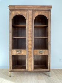 This beautiful art-deco arched glass and wood bookcase or curio cabinet is manufactured by the reputable B.P. John from Portland, Oregon. This piece is in such beautiful condition and the amazing arched doors and original brass hardware is a show-stopper for any style of home, office or commercial space. 