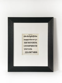 Corvinus Bold Vintage Industrial Font Alphabet Graphic Framed Art Framed in a modernized black frame with white mat. The alphabet fonts and numbers are featured on an antiqued page of type and lettering for typographers, letterers and designers published in 1950. 