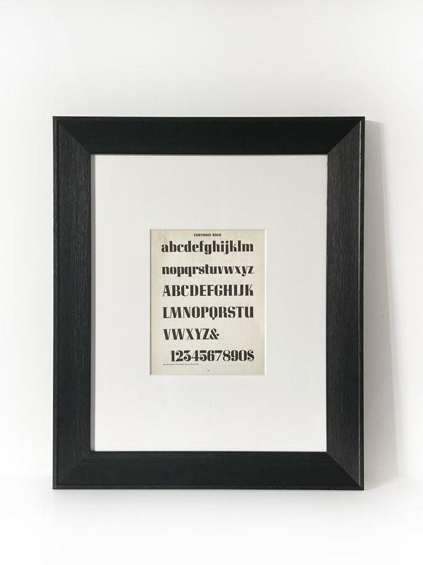 Corvinus Bold Vintage Industrial Font Alphabet Graphic Framed Art Framed in a modernized black frame with white mat. The alphabet fonts and numbers are featured on an antiqued page of type and lettering for typographers, letterers and designers published in 1950. 